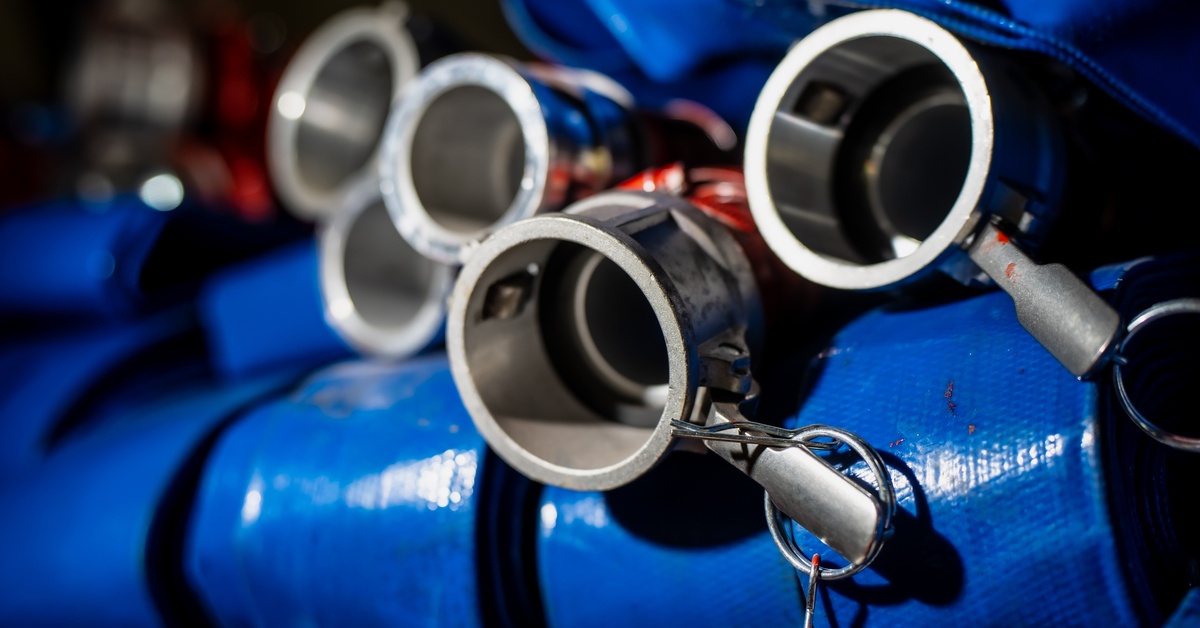 A closeup of the ends of several large, blue hoses. The hoses end in stainless steel camlock fittings.