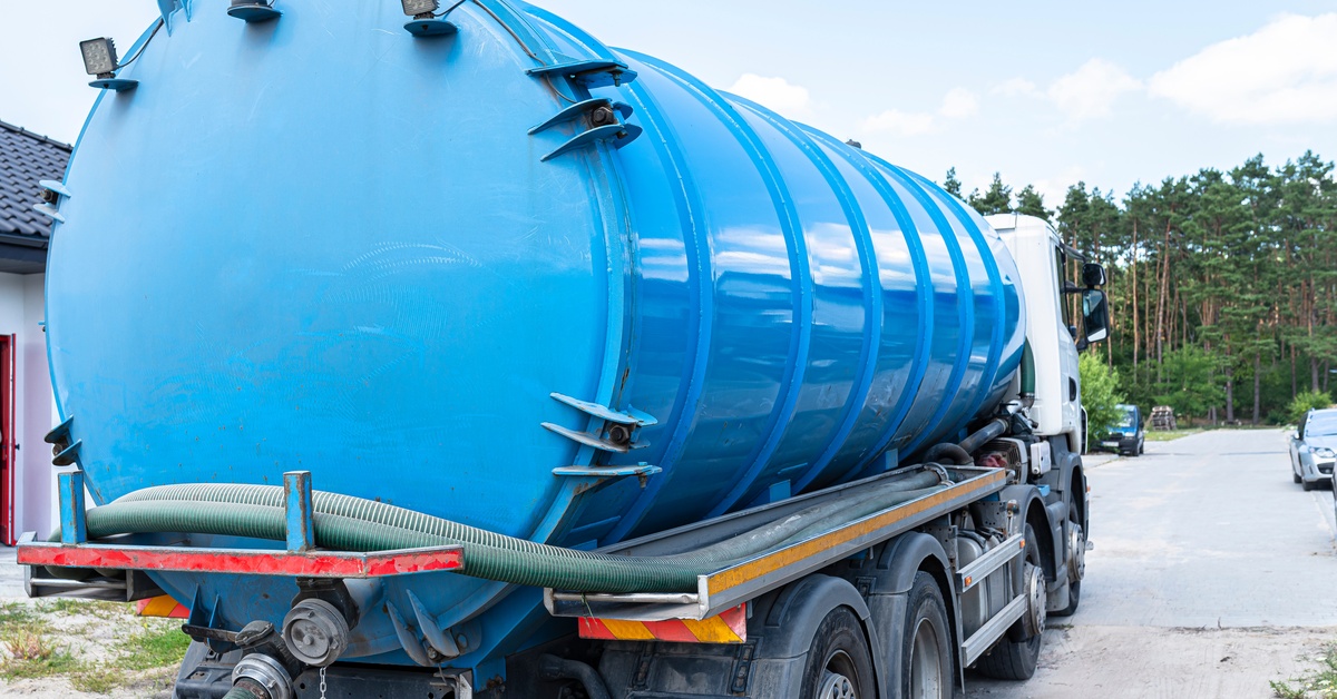 A close-up of the back of a blue septic truck with a teal vacuum pump attached. It's parked on a driveway.