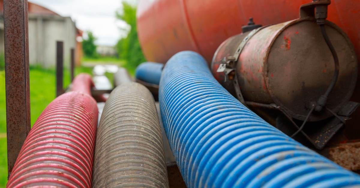 A close-up of a red, blue, and white vacuum pump attached to a septic truck. The truck is in a residential neighborhood.