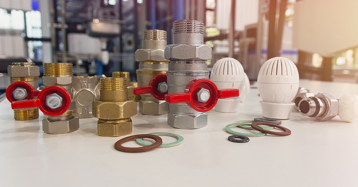 An assortment of valves, fittings, and rubber seals on a table. There is a factory setting in the background.