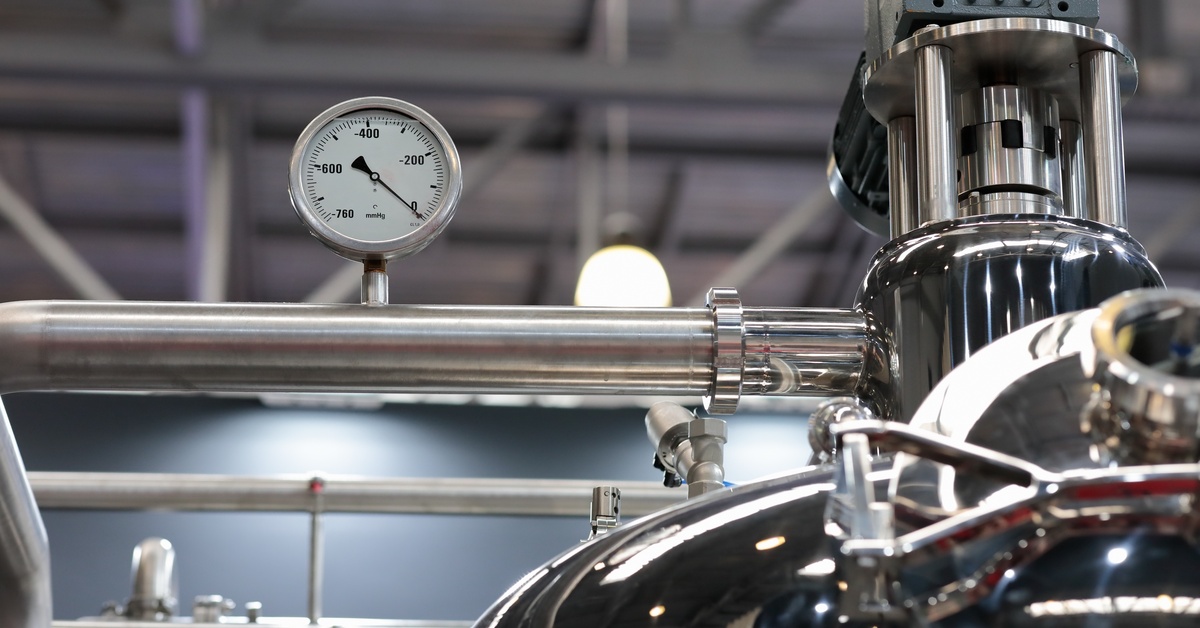 A large piece of stainless steel equipment. There is a small vacuum gauge on the piping of the machinery.