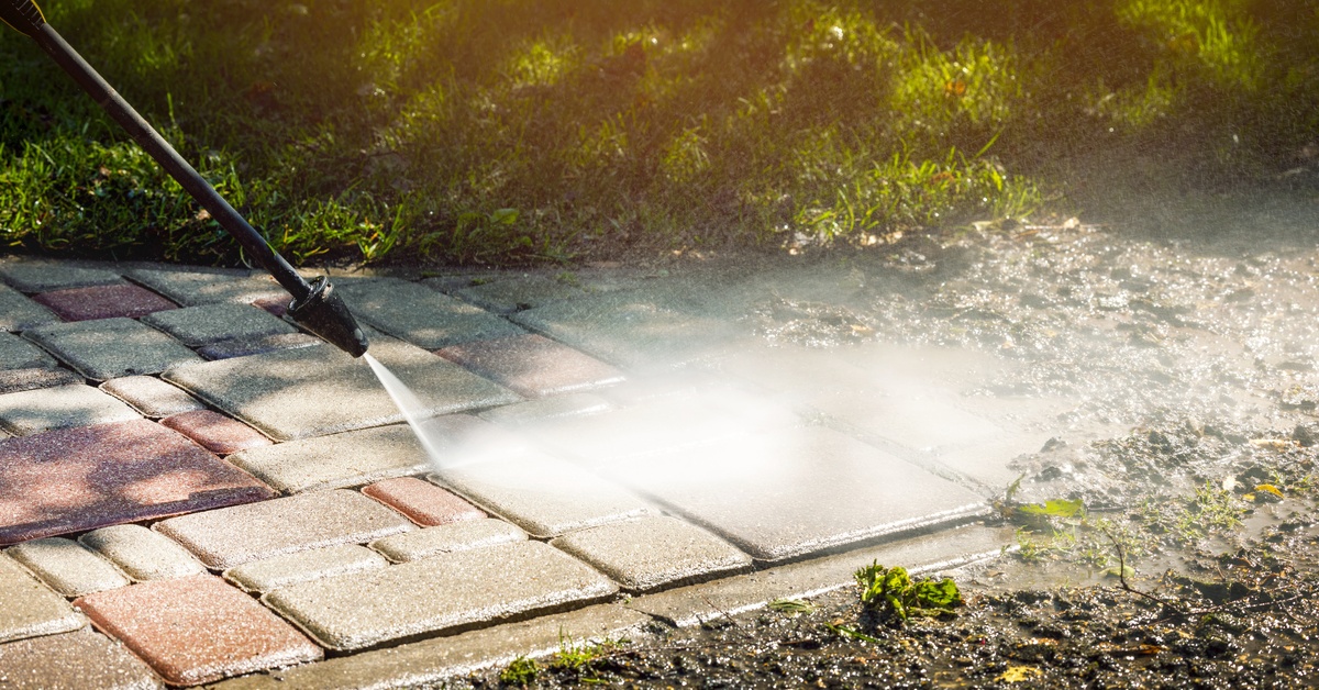 A dirty stone pathway is being cleaned by a pressure washer. The spray is heavily angled to get between the stones.