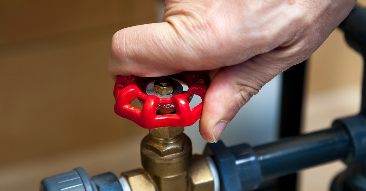 A closeup of a hand tightening the knob of a valve. The valve is in the middle of a plastic pipe system.