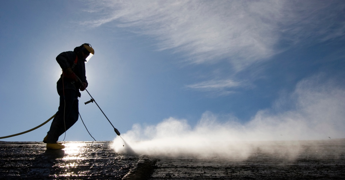 The silhouette of a pressure washer professional in a full safety suit against the backdrop of a slightly cloudy sky.
