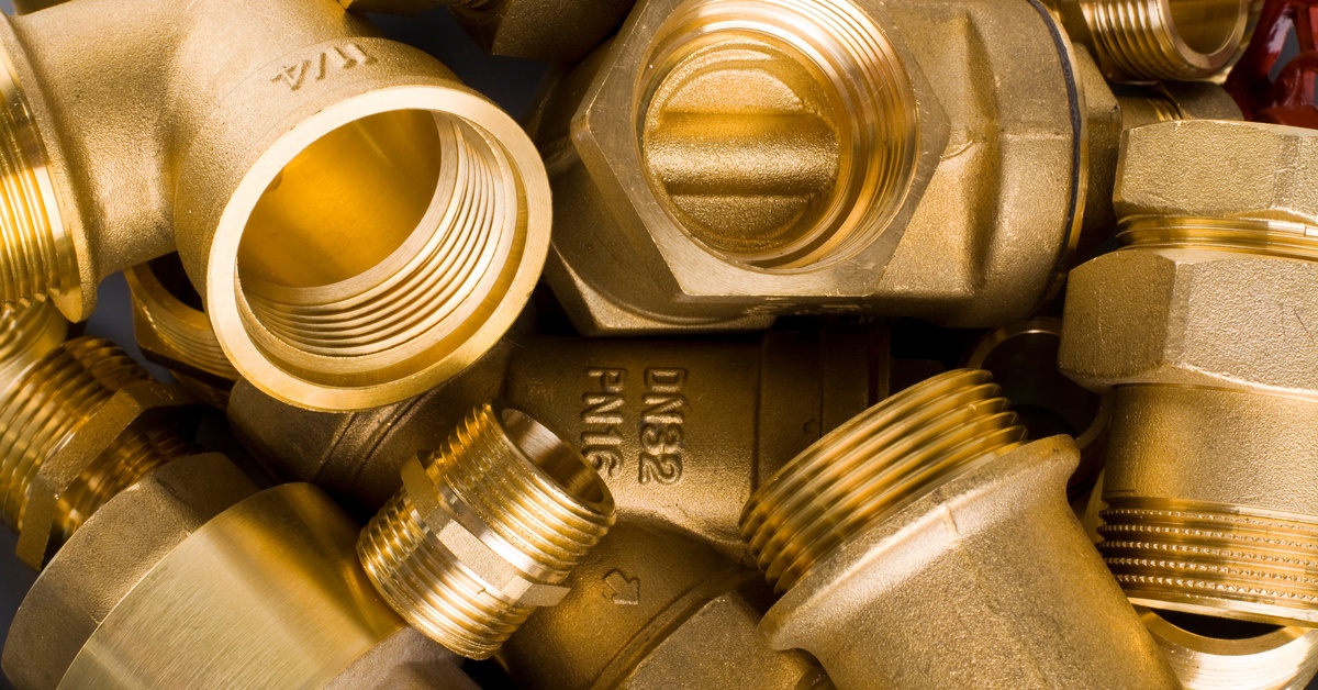 A collection of brass fittings piled on top of one another. Some of them have numbers and letters embossed on them.