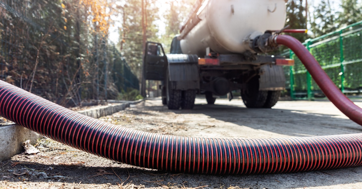 A close up of a red and black banded hose that travels back toward a white sewage truck in the background.