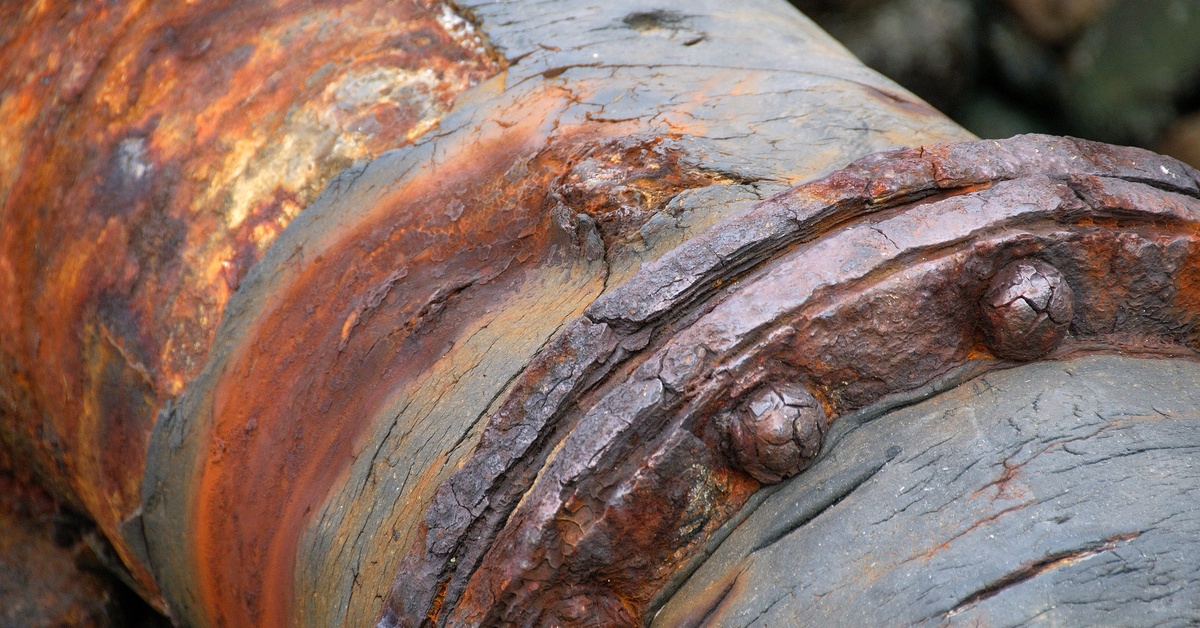 A closeup of a large pipe that is completely covered in corrosion and rust. Part of the pipe is bulging out.