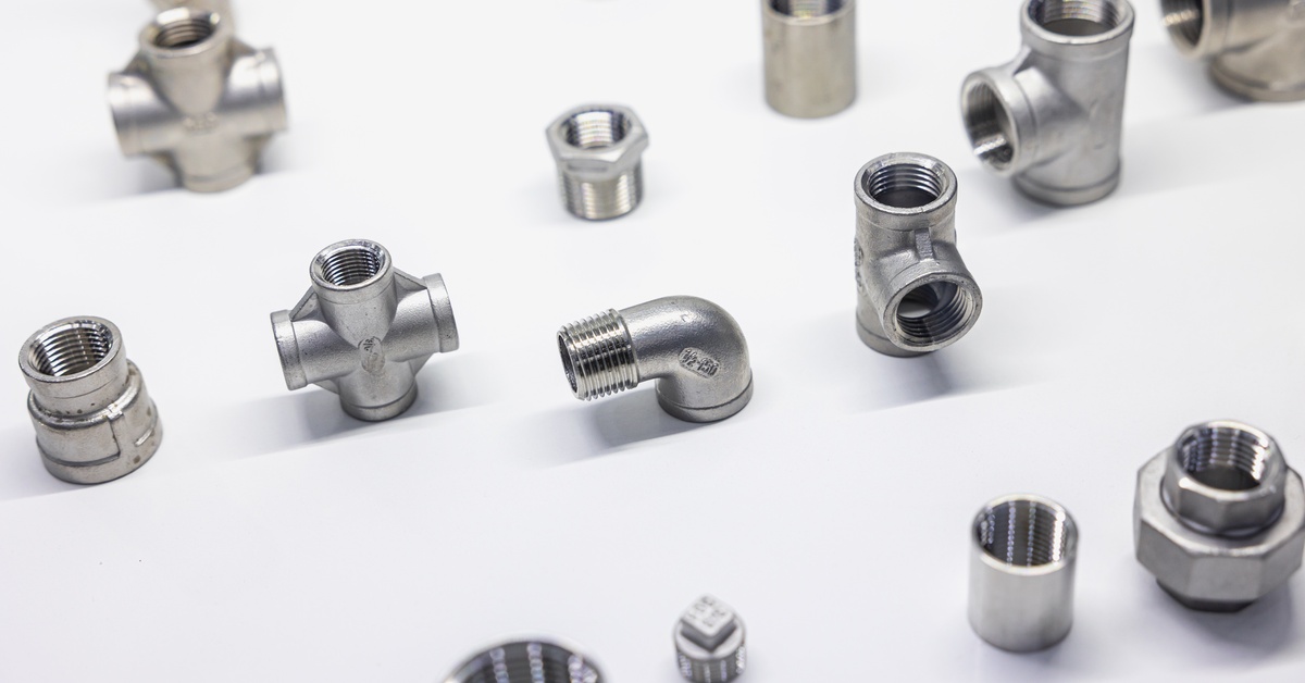 A collection of small metal pipe fittings on a white background. The fittings come in multiple shapes.