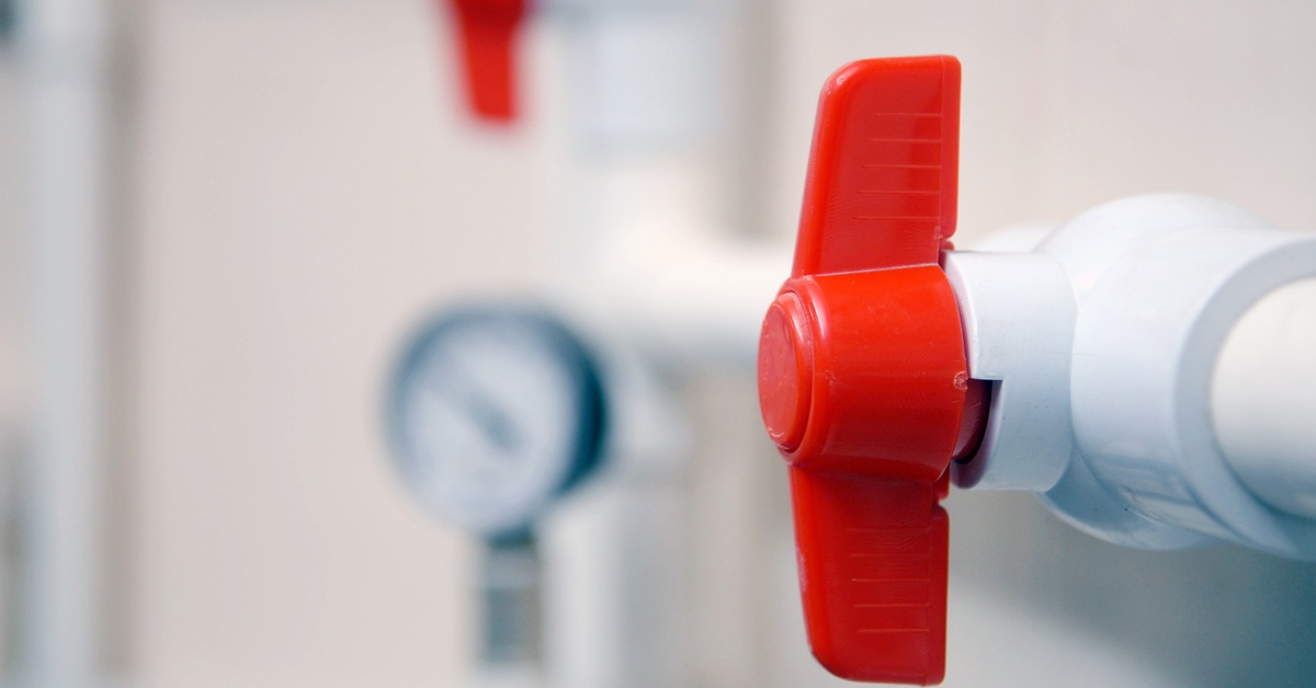 A closeup on a red, plastic valve attached to the side of some plastic piping. The piping blurs off in the distance.