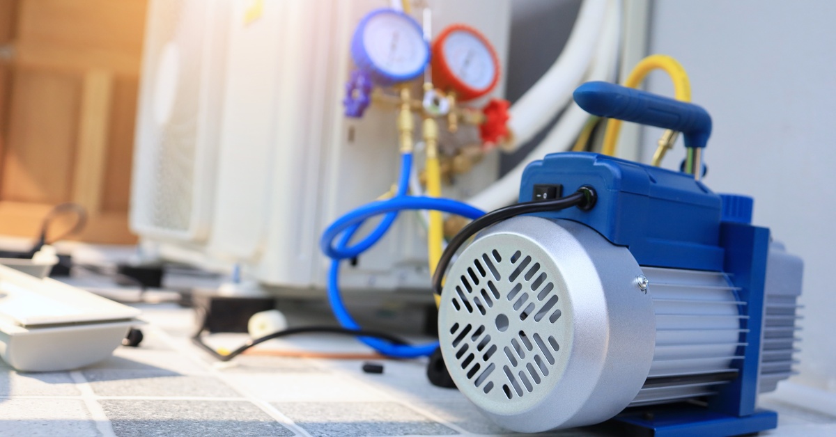 A blue and silver vacuum pump sitting on a tiled floor. The pump is hooked up to two gauges that are in the background.