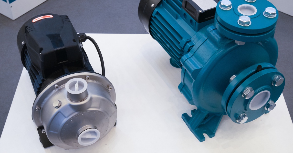 Two electric, portable water pumps on a white podium. One pump is black plastic while the other one is a blue metal.