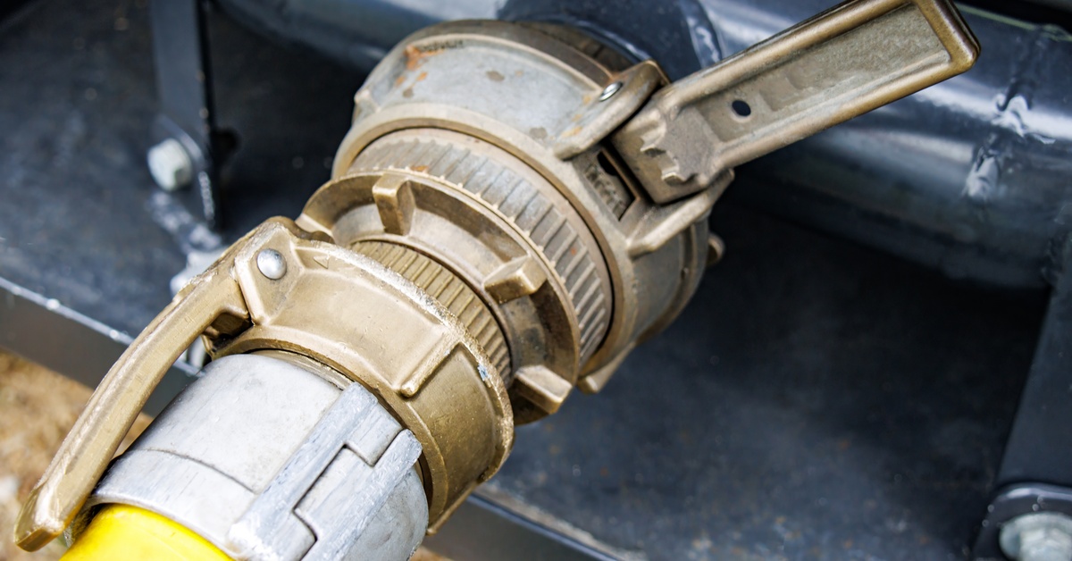 A closeup on a camlock fitting that is connected to a hose on one end and some industrial equipment on the other.