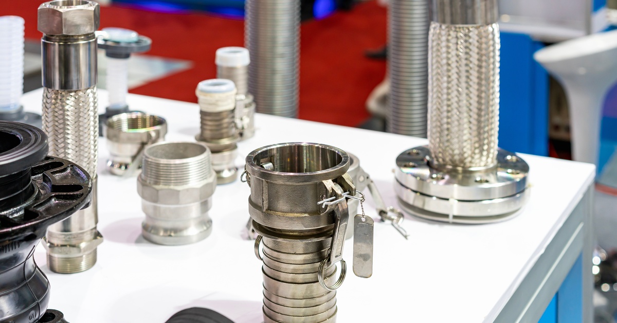 A collection of different sized metal fittings. A camlock fitting is sitting next to other fittings on a white table.