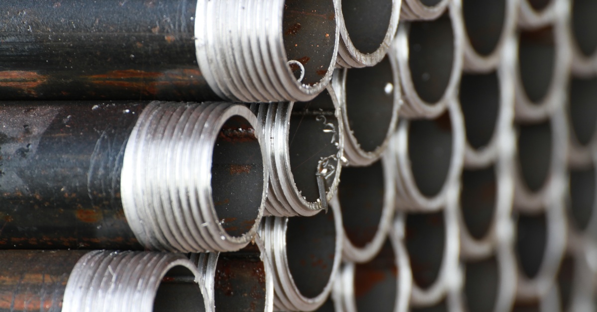 A large stack of painted black pipes piled on top of one another. Their threaded ends are all pointing out.