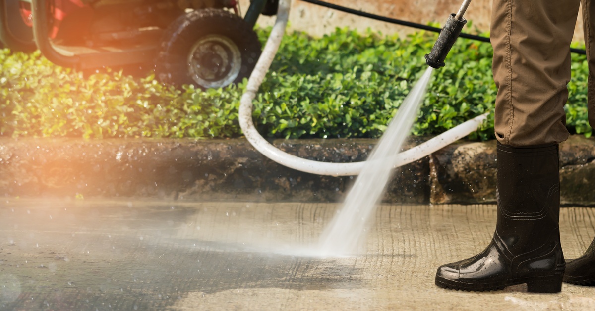 A closeup on the end of a pressure washing hose as it is spraying water. The washing machine is on the grass behind it.