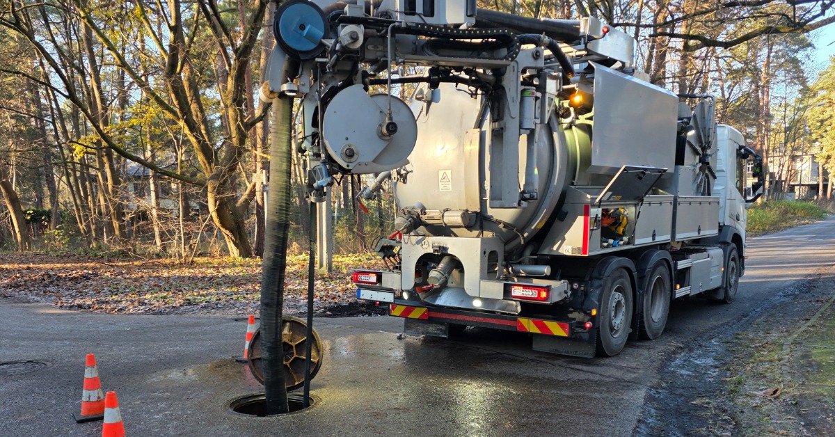 A gray hydrovac sewer cleaning truck parked on the street. The large hose attached to it is going into a manhole.