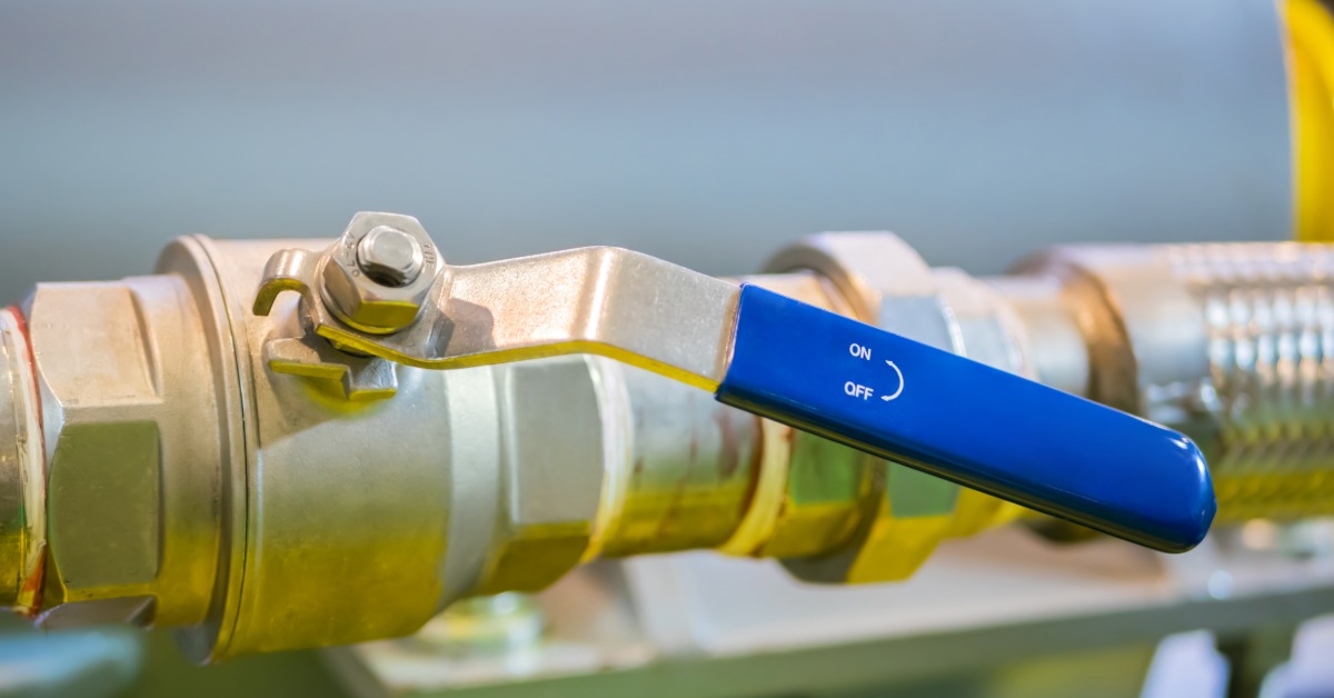A closeup on a brass ball valve with a handle sticking out of it. The handle has arrows that point to on and off.