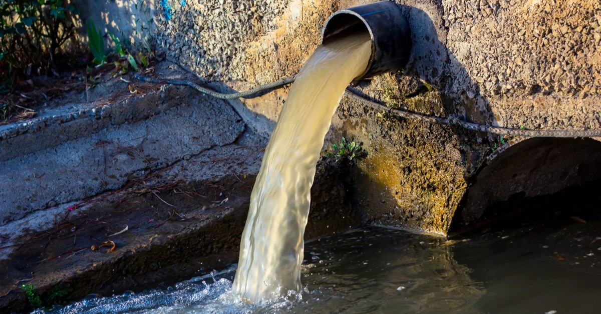 A spout of wastewater coming out of a pipe in the wall. The water is falling into a larger current of wastewater.