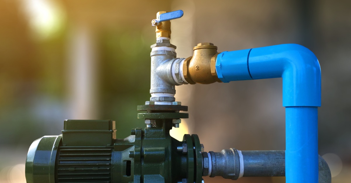 A closeup on a water pump system with multiple pipes leading out of it. There is a control handle on the top of the system.