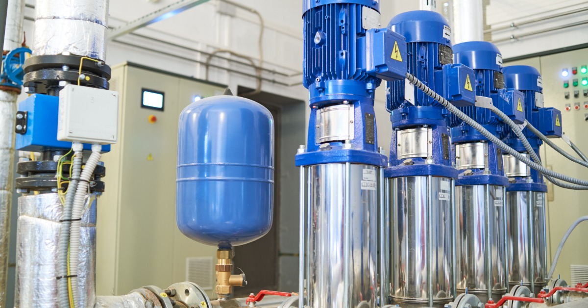A series of pipes and valves in a water pump system. A large water tank is positioned on the top of the system.