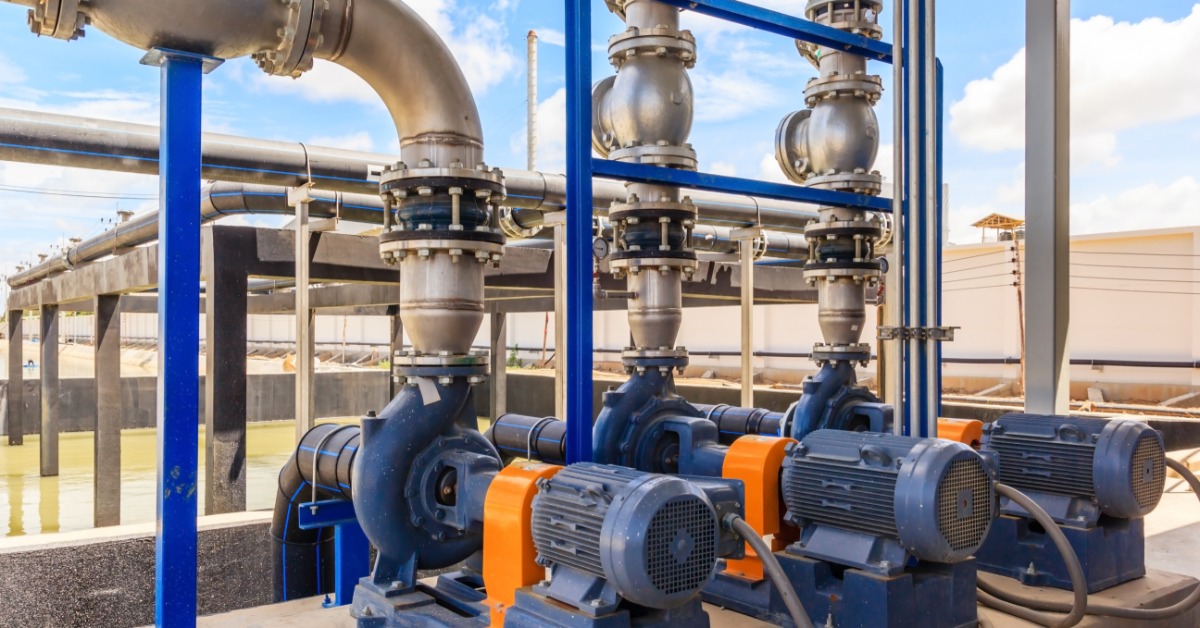 Three large, blue wastewater pumps lined up next to each other with multiple pipes going in and out of them.
