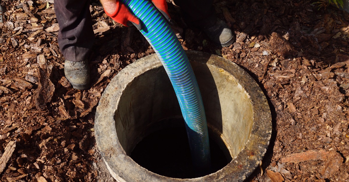 A sewage worker feeding a large blue hose down into a hole in the ground to start pumping water out of it.