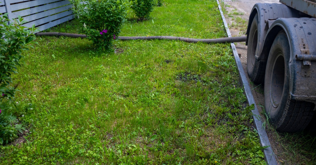 A septic service truck parked next to a house's lawn. There is a hose going from the truck to the house.