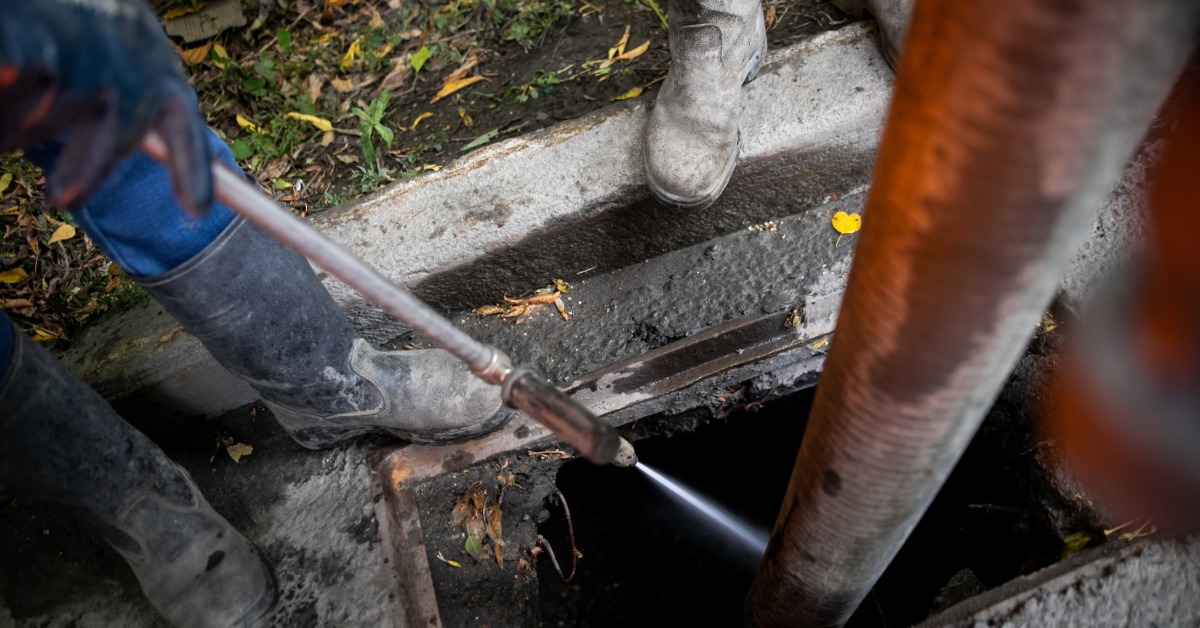 A sewer professional using a long hose to clean off debris from inside of a storm drain. Water is coming out of the hose.