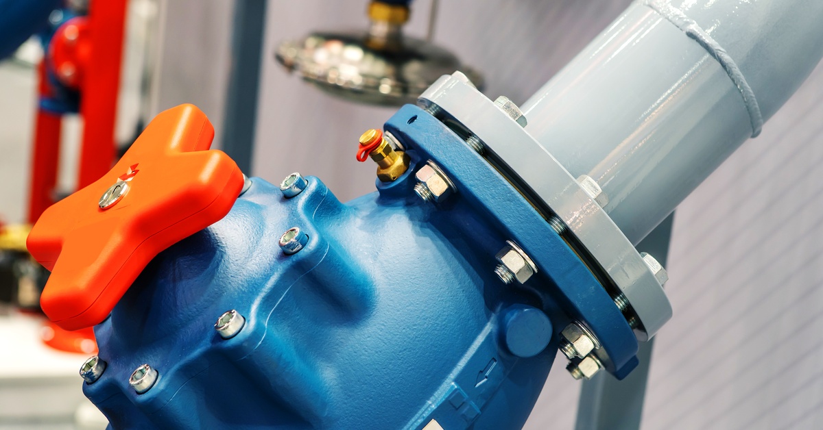 A close-up shot of a large blue plastic valve with an orange handle. It is attached to a metal pipe.
