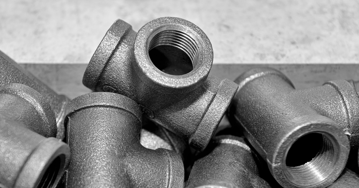 Several black steel pipe fittings in a tee shape piled up together against a gray stone background.