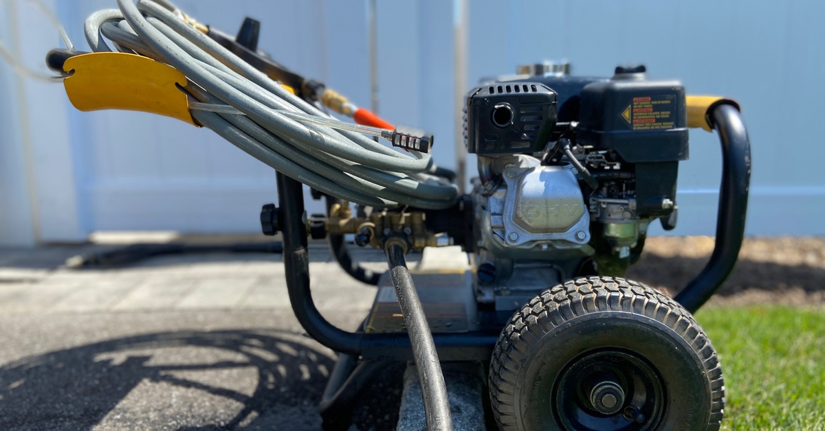 A side view of a pressure washing machine with a gray hose rolled up and another gray hose connected to an underside component.
