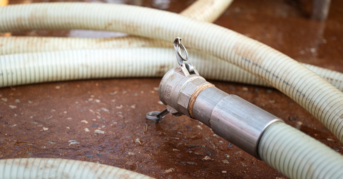 A close-up of a white water-jetting hose with a metal nozzle attached to it resting on a brown floor.