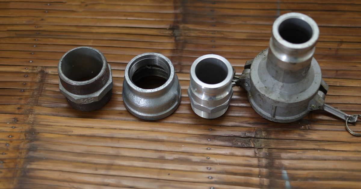 A line of four camlock couplings in various shapes and sizes are laid out on a textured wooden surface.