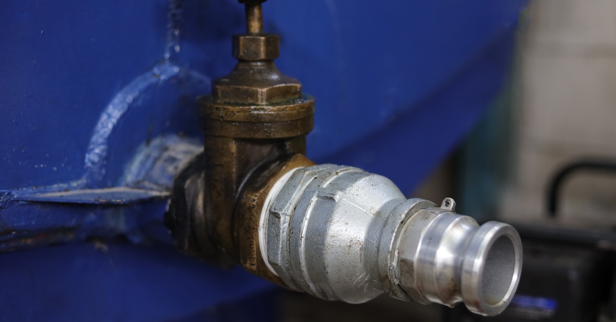 The drainage attachment on a blue tank with a camlock coupling and a red valve handle on top to control flow.
