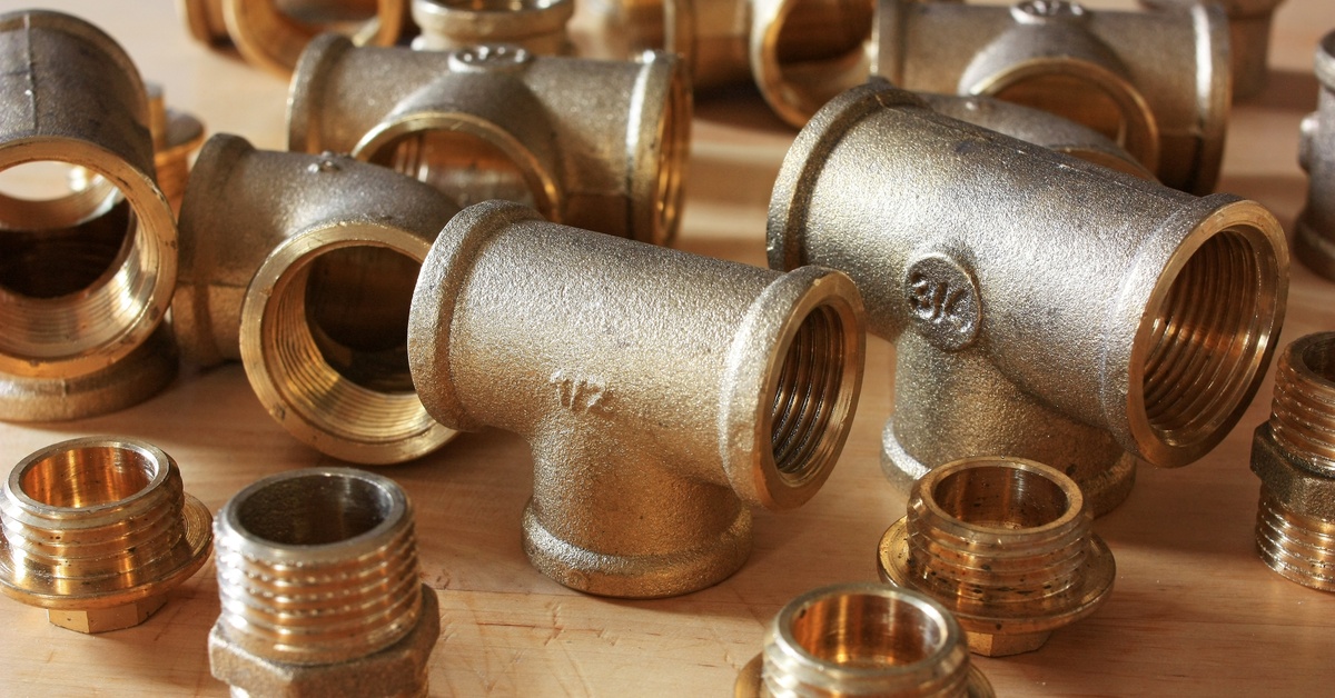 A collection of shiny and new brass pipe fittings of different shapes and sizes laid out on a wooden surface.