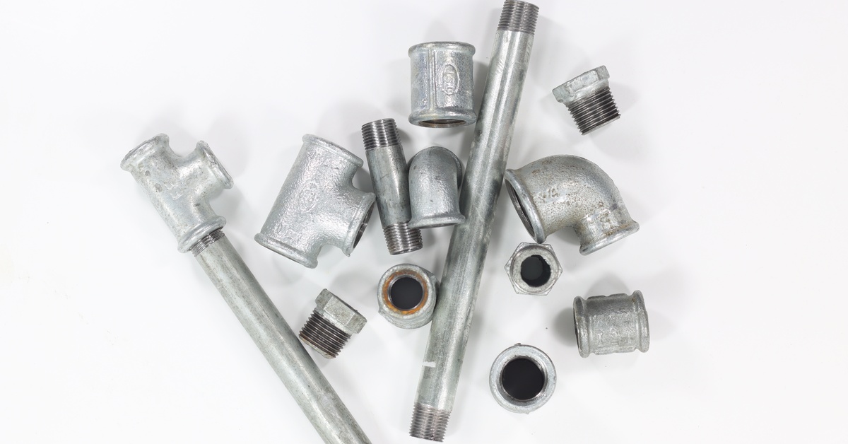 A cluster of metal pipe fittings on a white surface including tees, elbows, fasteners, straight pipes, and caps.
