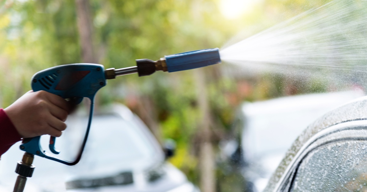 A person holding a blue pressure washer gun while squeezing the trigger and causing it to project a stream.