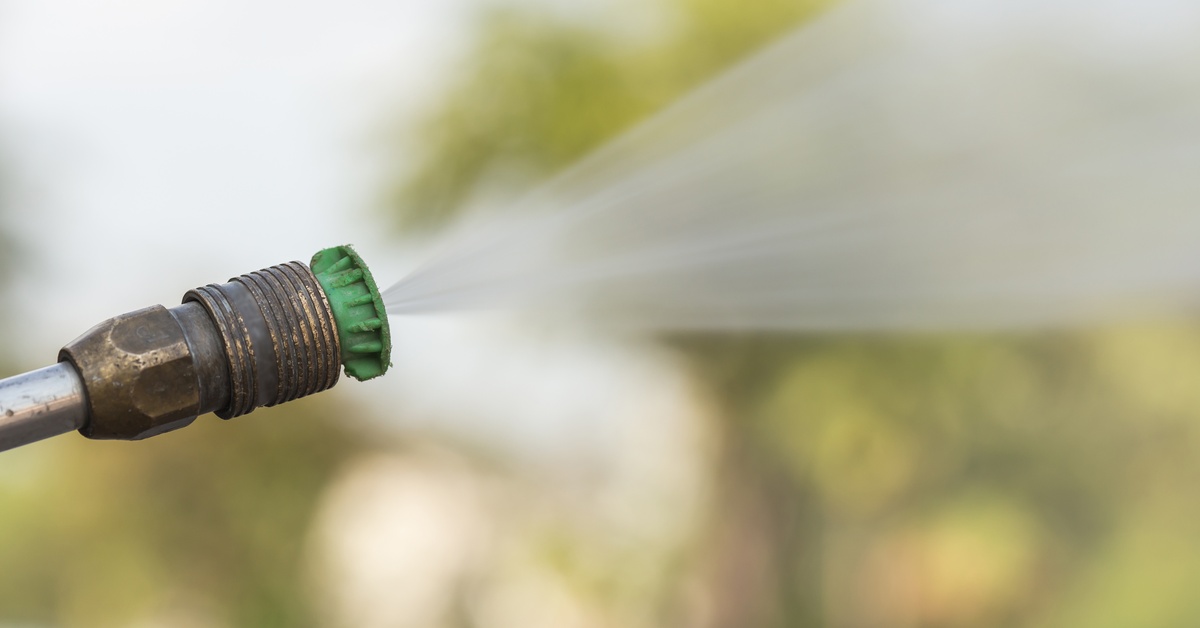 The nozzle of a pressure washer with a green tip and rusted metal sprays a stream of water in an outdoor area.