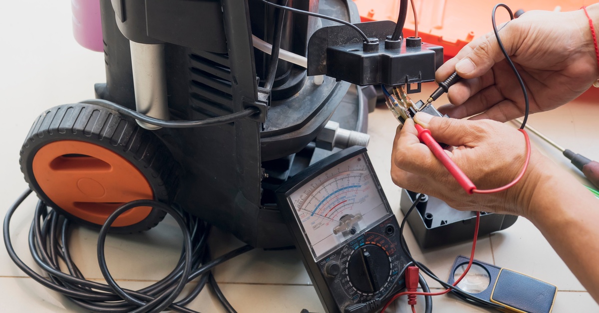 A person tinkering with the electrical components of a pressure washer with a multimeter nearby to measure voltage.