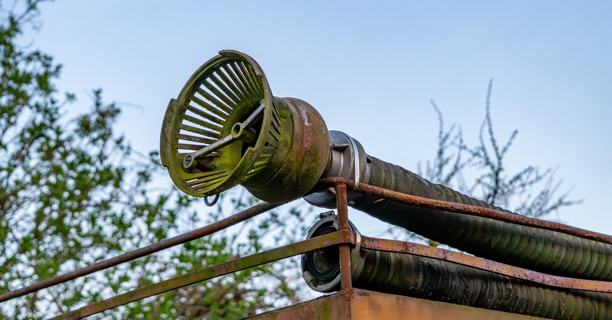 A old, rusted suction hose on top of the rail on a worn metal structure with a smaller hose laying underneath it.