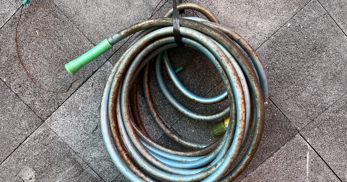 A coiled blue hose hanging from a cord on a concrete wall. The hose's exterior is corroded.