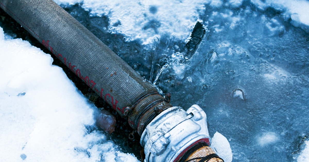 A hose with two sections connected via couplings leaks water onto the icy ground due to punctures in its surface.