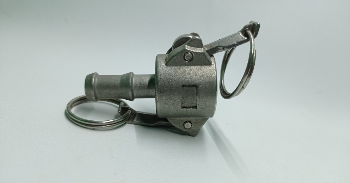 A stainless-steel Camlock coupling placed on its side as one of its couplings points right on a gray surface.