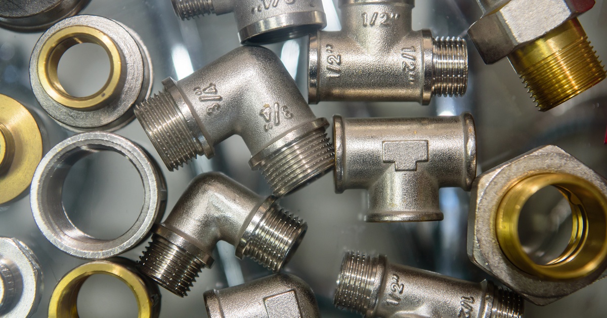 Multiple brass pipe fittings including tee valves, rings, and elbows placed on a transparent surface.