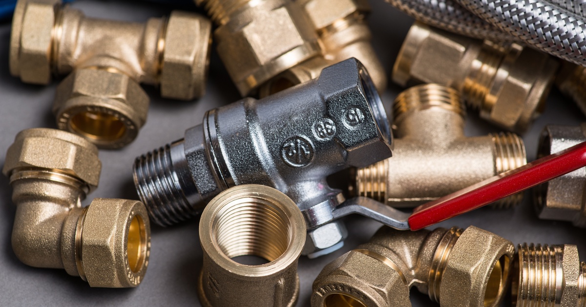 A collection of brass pipe fittings and joints placed on a white surface with an iron faucet with a valve handle in the center.