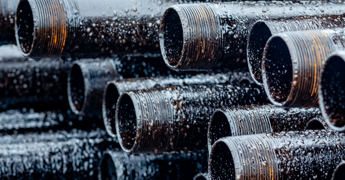 A stacked pile of pipes with threaded ends left in the rain with droplets falling down their surfaces.