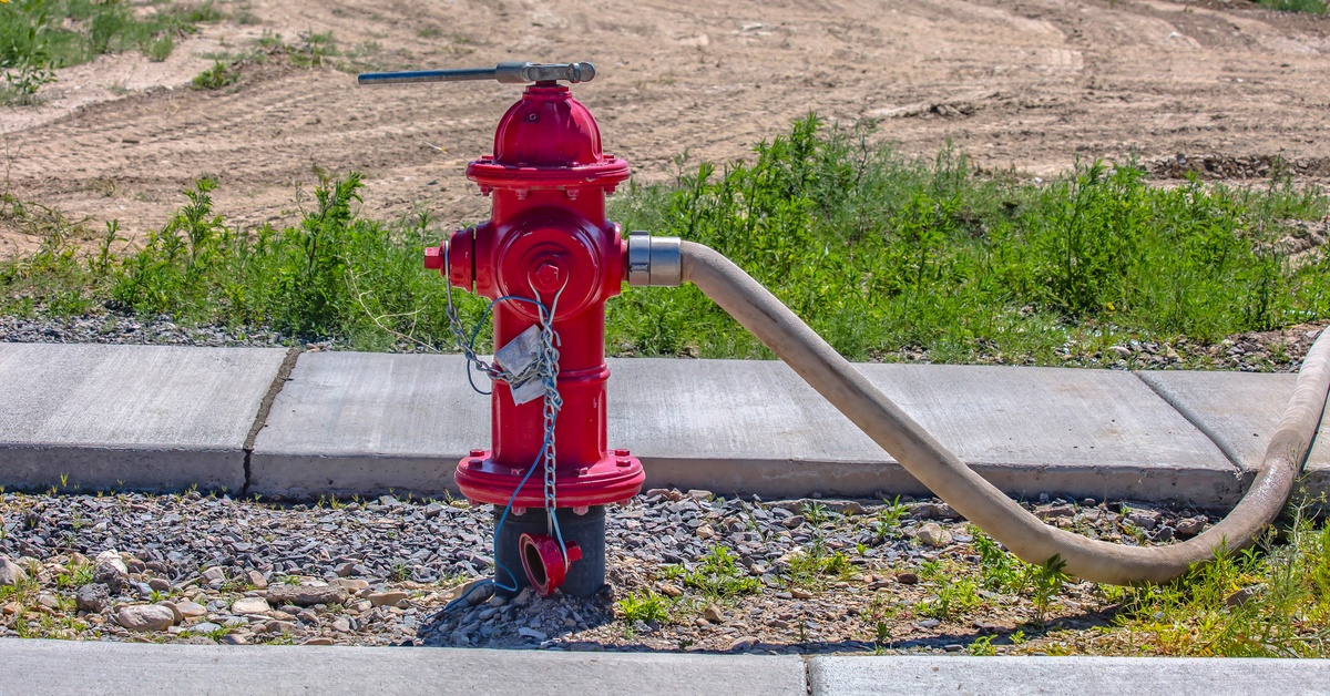 A fire hydrant with an attached hose next to a row of cement blocks that form a sidewalk and a barren area.