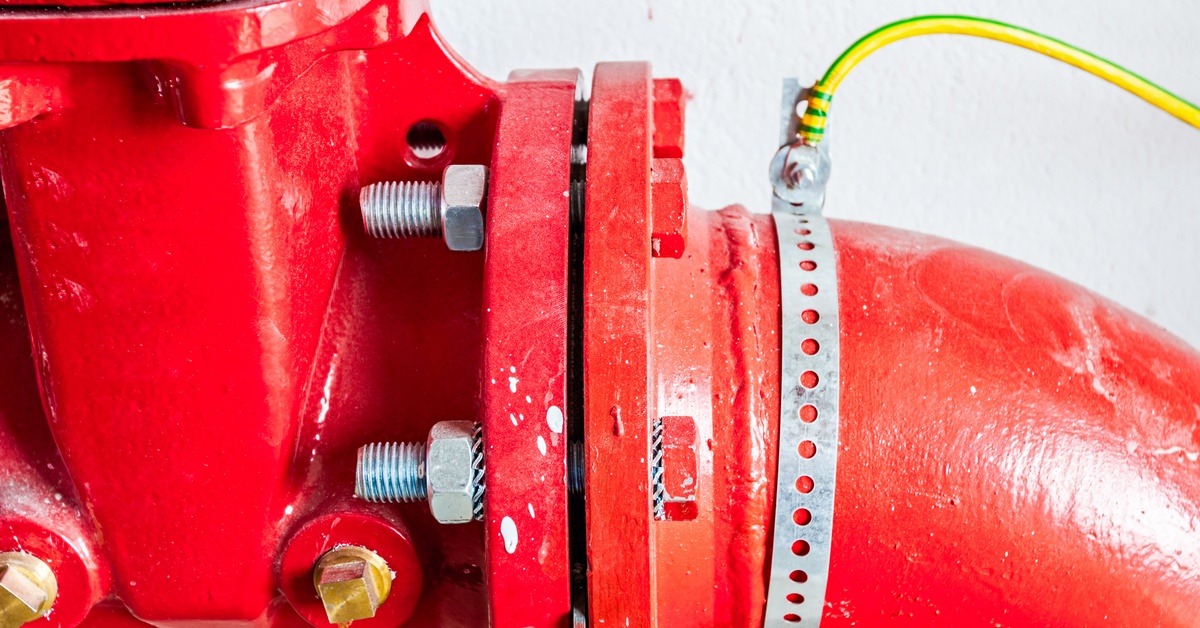 A bright red fire hydrant with an attached elbow adapter pointing down at an angle with bolts to keep it in place.